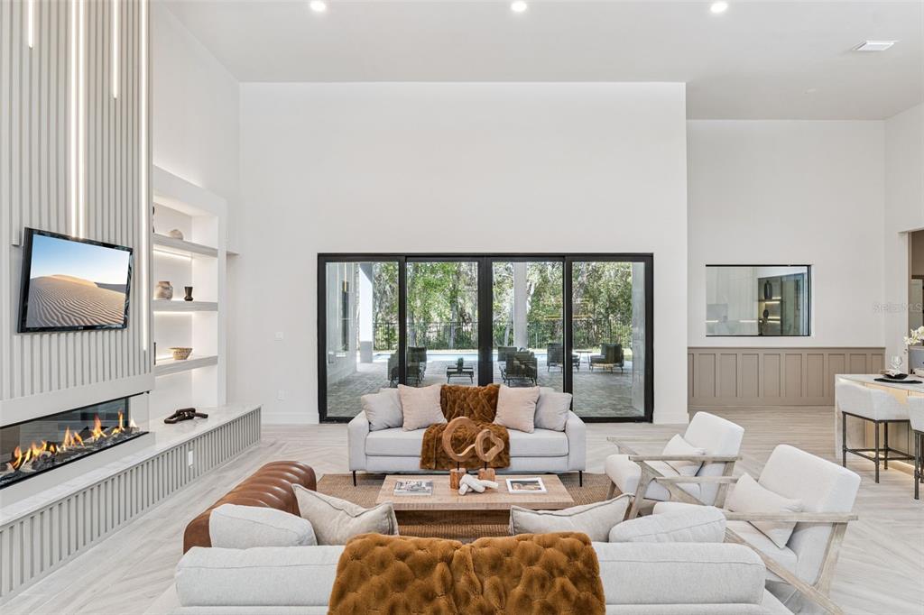 A modern living room features a linear fireplace, tall ceilings, and large sliding glass doors — 1447 BIRD ROAD, WINTER SPRINGS, FL