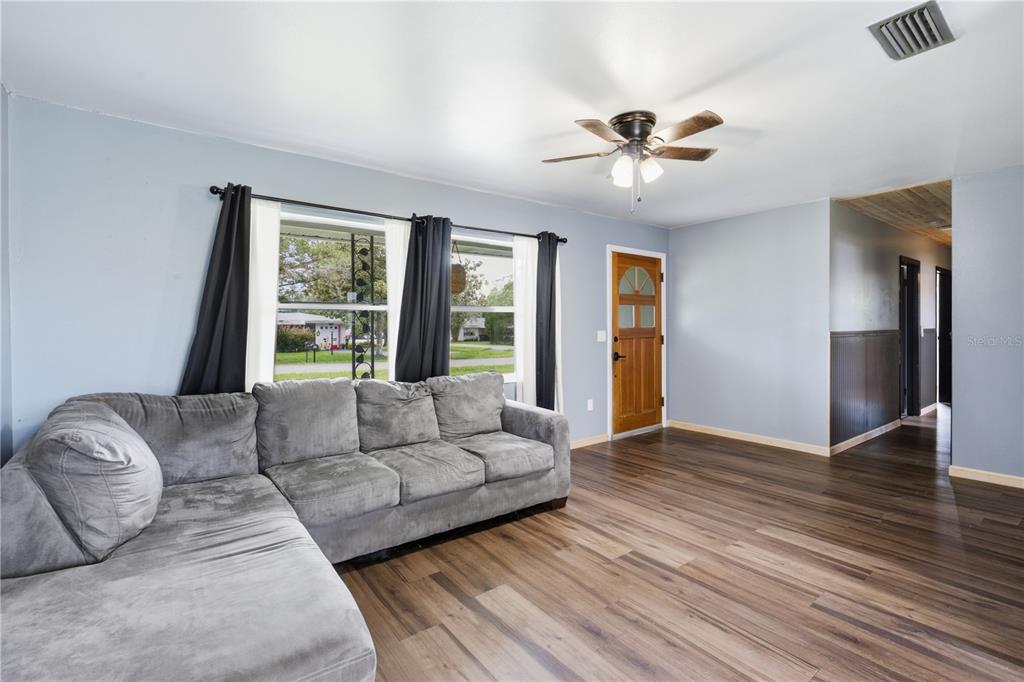 A living room with light blue walls, wood-look flooring, a gray sectional sofa, and ceiling fan — 5307 SE 108TH STREET, BELLEVIEW, FL