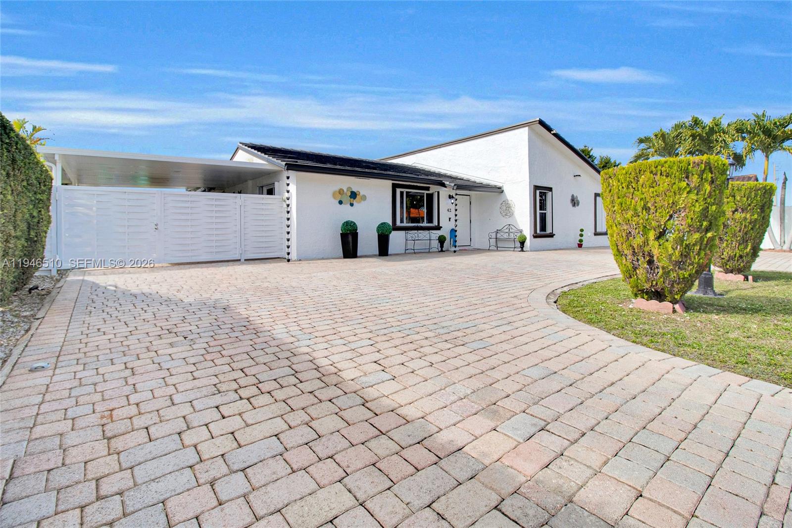 A white single-story house features a large paver driveway and a covered carport area — 42 NW 132nd Pl, Miami FL 33182, MIAMI, FL