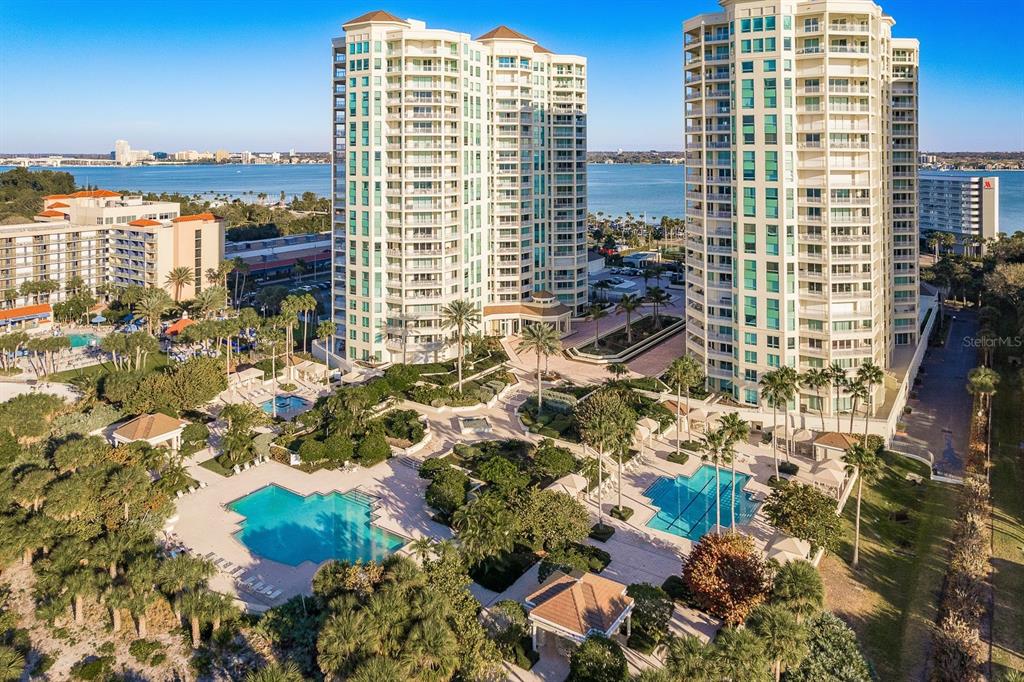 An aerial view shows two tall residential towers with swimming pools and landscaped grounds — 1170 SE GULF BOULEVARD UNIT 305, CLEARWATER BEACH, FL