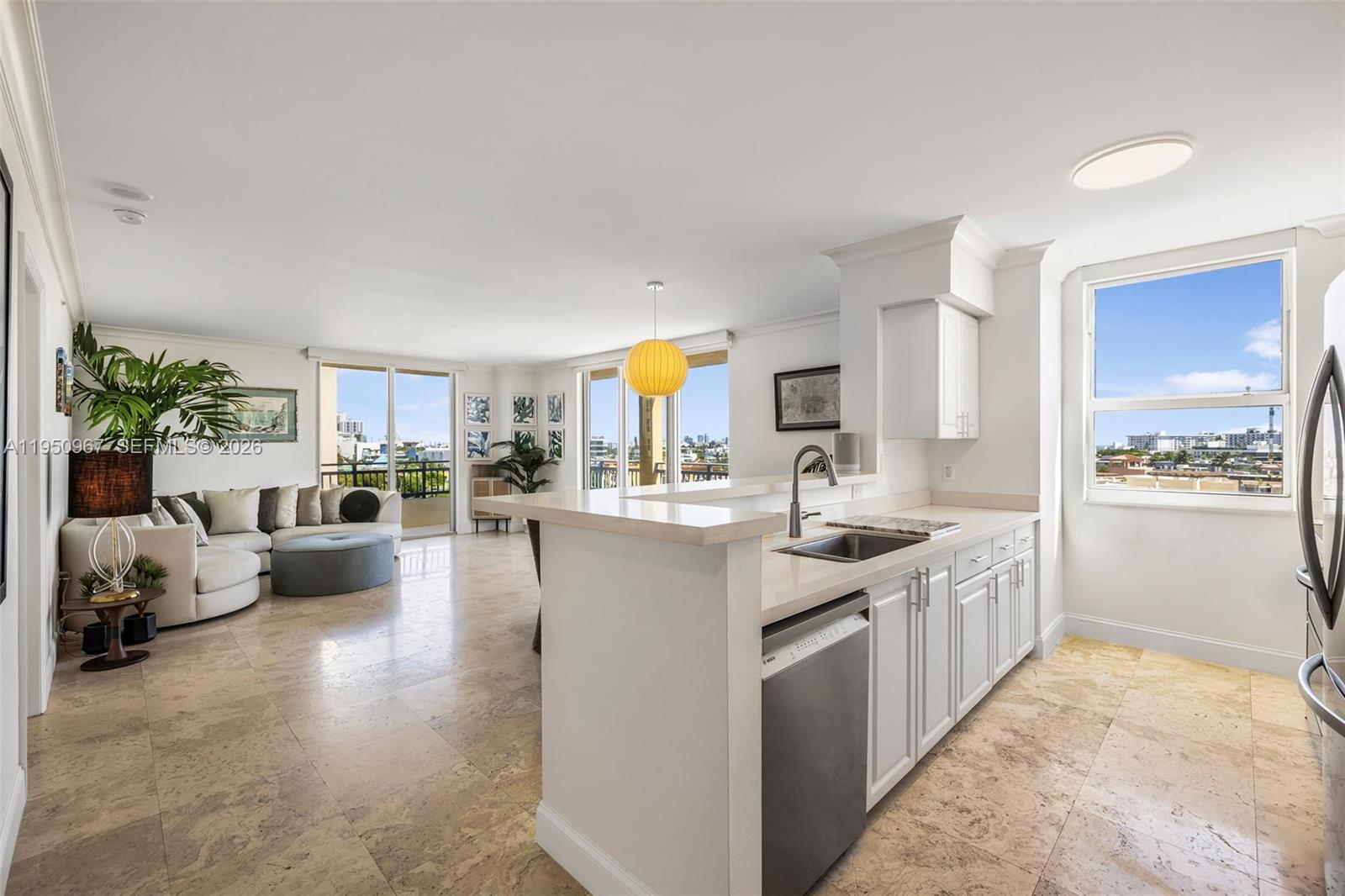 A kitchen with white cabinets and a breakfast bar overlooks an open-concept living area — 90 Alton Rd # 811, Miami Beach FL 33139, MIAMI BEACH, FL