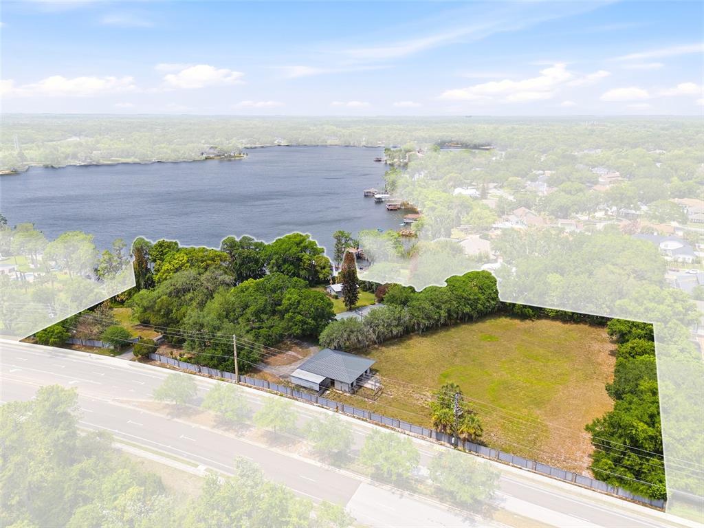 An aerial view shows a house and a large vacant lot bordering a lake — 4910 E LAKE DRIVE, WINTER SPRINGS, FL