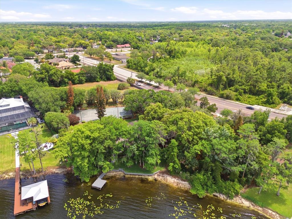An aerial view shows a waterfront property with a dock, tennis court, and dense trees — 4910 E LAKE DRIVE, WINTER SPRINGS, FL