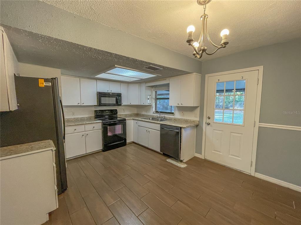 A kitchen features white cabinets, granite countertops, stainless steel appliances, and light wood-look tile flooring — 9875 W ORCHARD STREET, CRYSTAL RIVER, FL