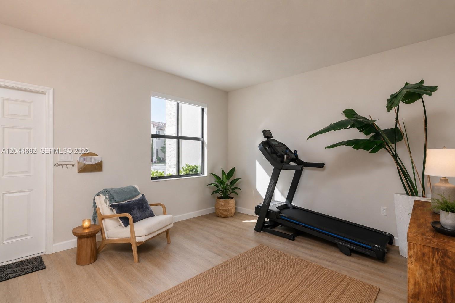 A room with light wood flooring, a treadmill, an armchair, and a large potted plant — 10079 SW 228 # 10079, Miami FL 33190, MIAMI, FL