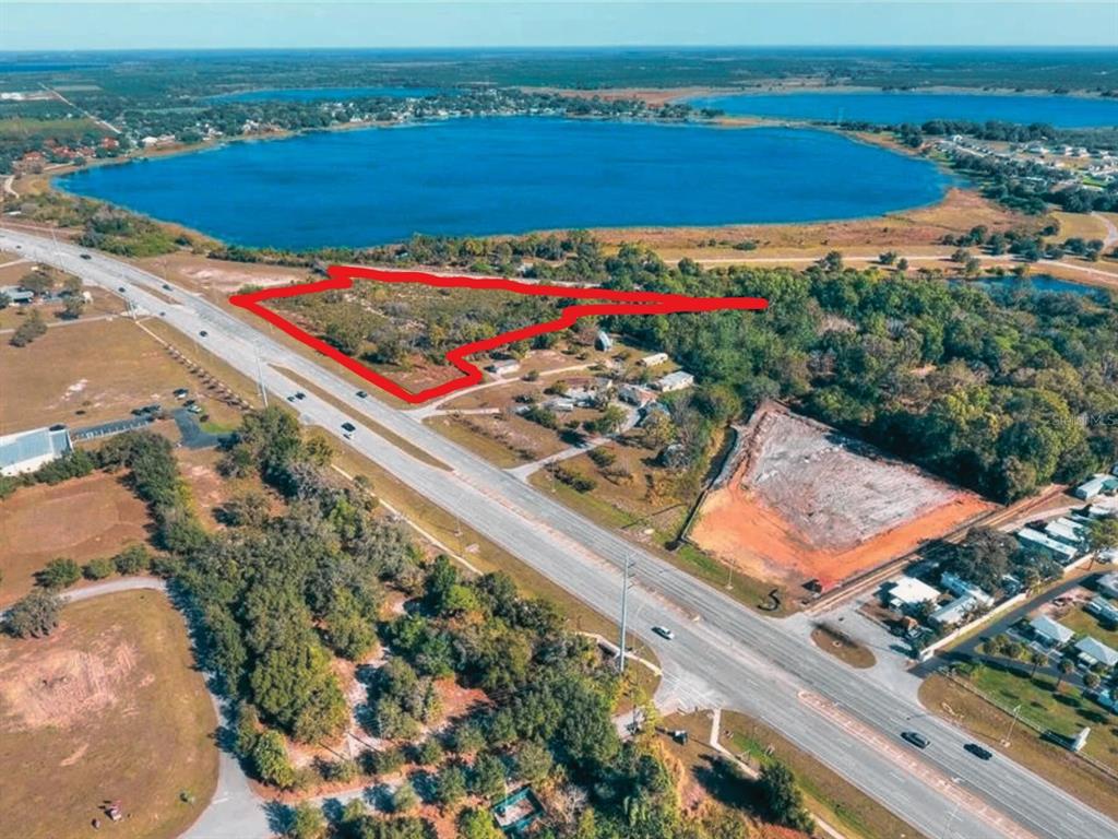 An aerial view shows a vacant, red-outlined plot of land adjacent to a highway and lake — 2210 US HIGHWAY 27 N, AVON PARK, FL