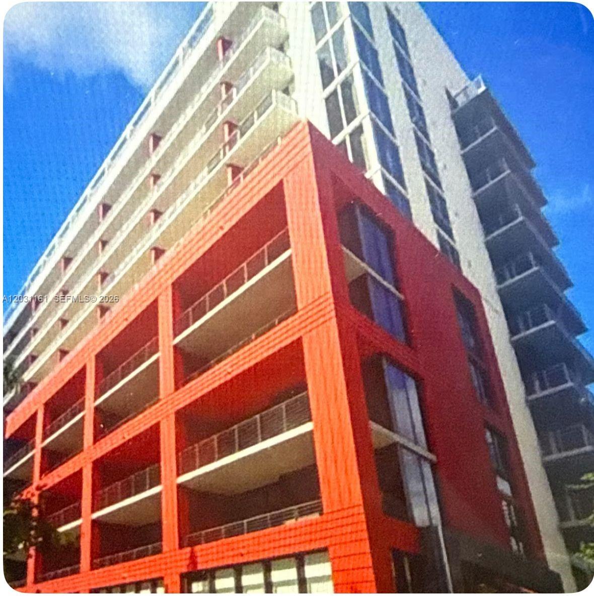 A low-angle view of a modern high-rise building featuring a prominent red exterior facade — 90 NE 32nd St # 624, Miami FL 33137, MIAMI, FL