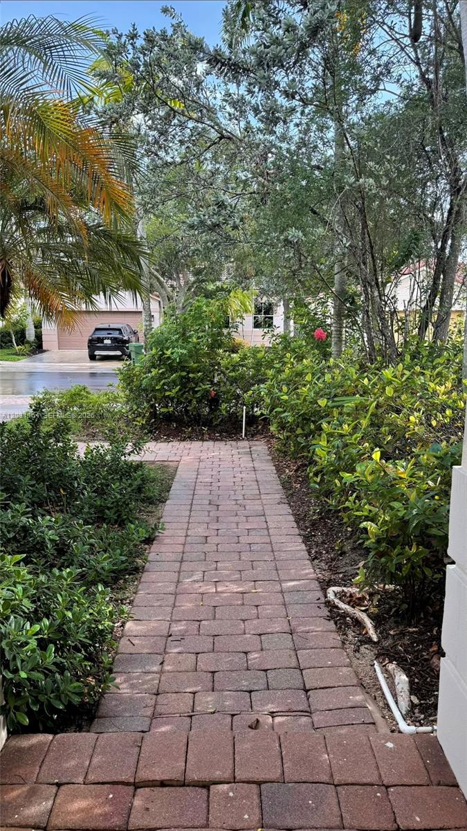 A brick walkway leads through a landscaped yard toward a house with a parked car — 748 Tulip Cir, Weston FL 33327, WESTON, FL