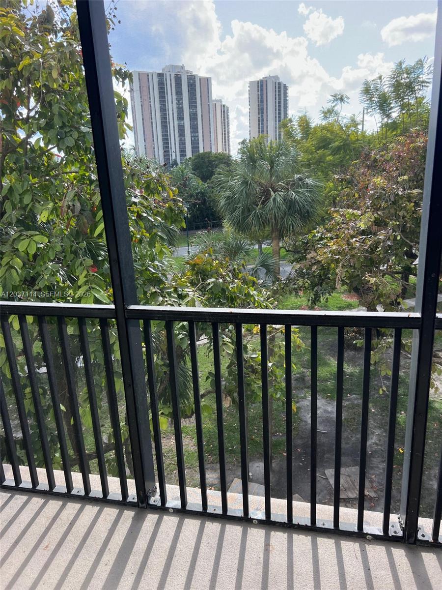 A view from a screened balcony overlooking trees, a grassy area, and tall apartment buildings — AVENTURA, FL