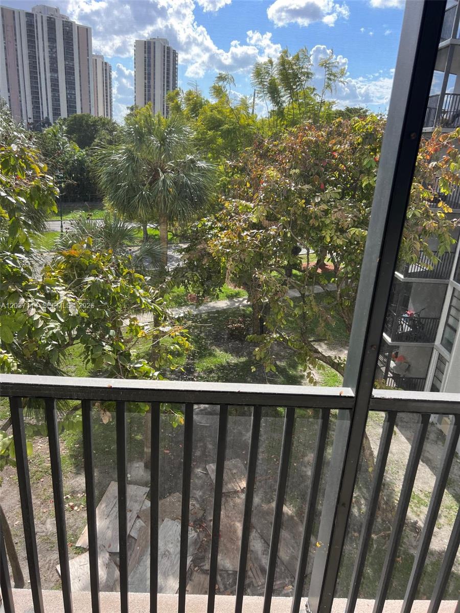A view from a balcony overlooking a grassy courtyard with trees and tall apartment buildings — AVENTURA, FL