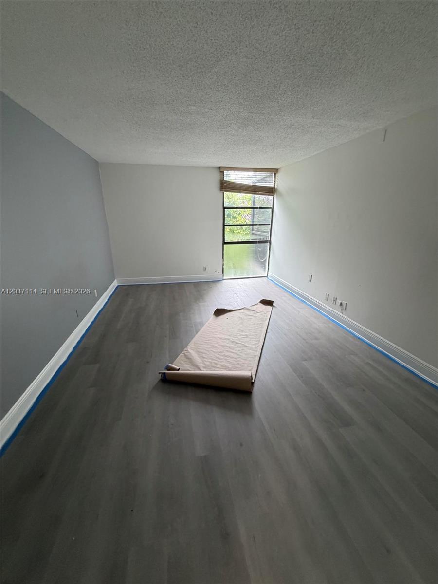 An empty room features gray wood-look flooring, white walls, and a tall window — AVENTURA, FL