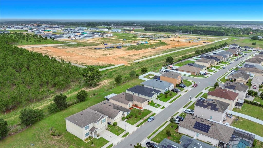 An aerial view shows a suburban neighborhood with houses bordering a large, undeveloped construction site — 357 NOVA DRIVE, DAVENPORT, FL