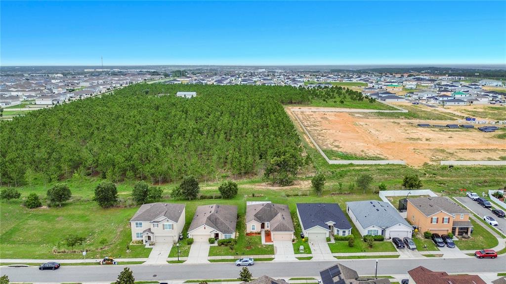 An aerial view shows a row of suburban houses bordering a large wooded area and construction — 357 NOVA DRIVE, DAVENPORT, FL