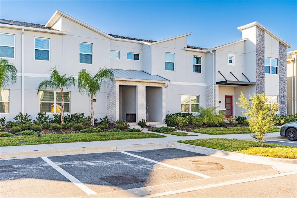 A two-story townhouse exterior with white siding, stone accents, and a paved parking area — 1146 KINGSBARN STREET, DAVENPORT, FL
