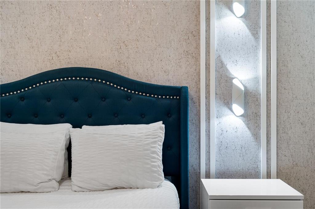 A bedroom features a tufted blue headboard, textured wallpaper, and wall-mounted lighting — 1146 KINGSBARN STREET, DAVENPORT, FL