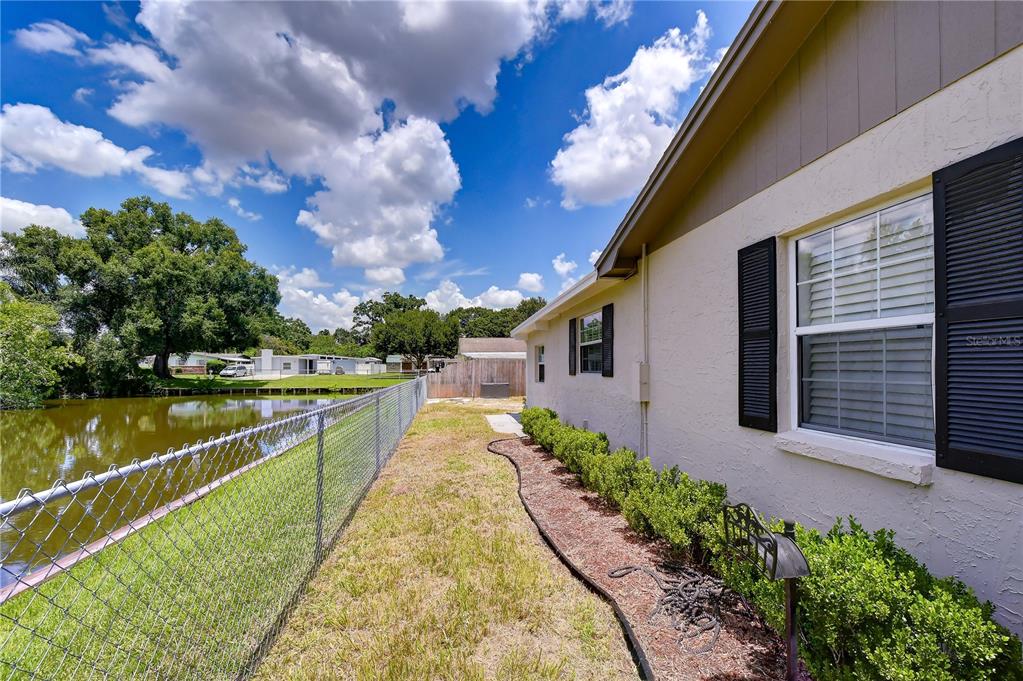A side view of a house exterior with a chain-link fence bordering a pond — 2101 W HAMILTON AVENUE, TAMPA, FL