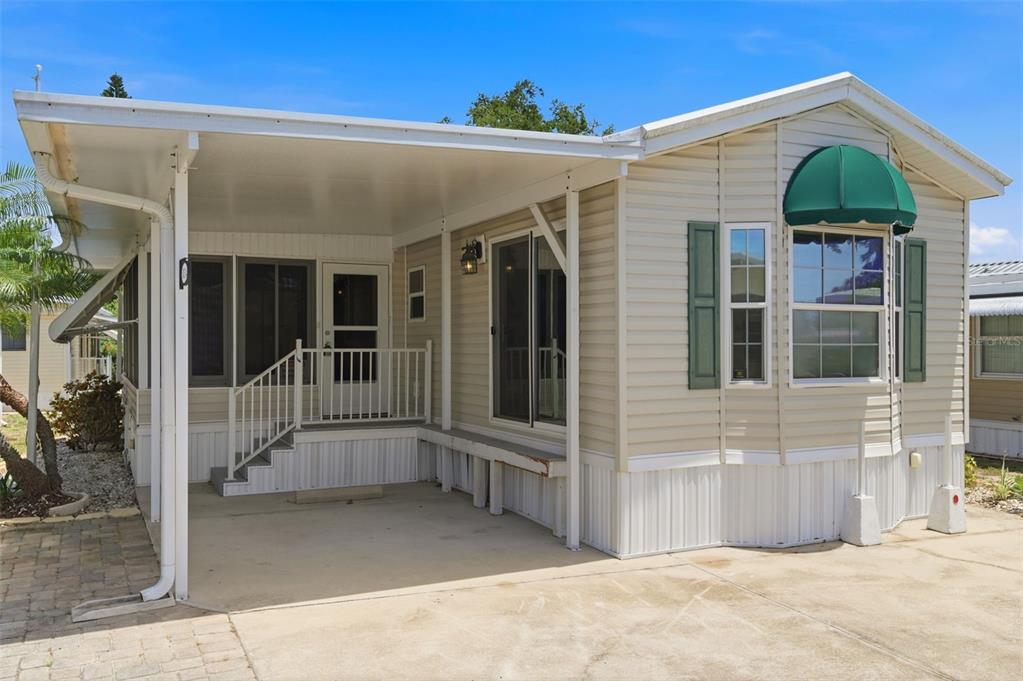 A beige manufactured home features a covered carport, a small front porch, and green shutters — 3275 26TH AVENUE E UNIT 134, BRADENTON, FL