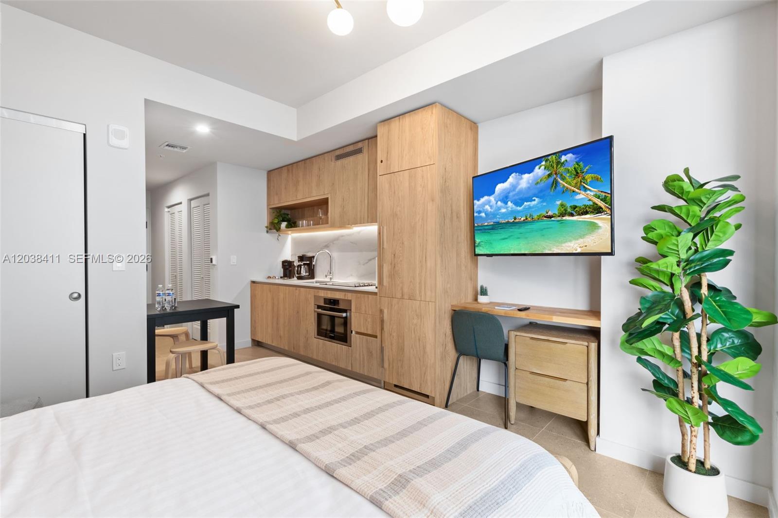 A studio apartment features a kitchenette with light wood cabinetry, a desk, and a bed — 11 NE 6th St # 2406, Miami FL 33132, MIAMI, FL