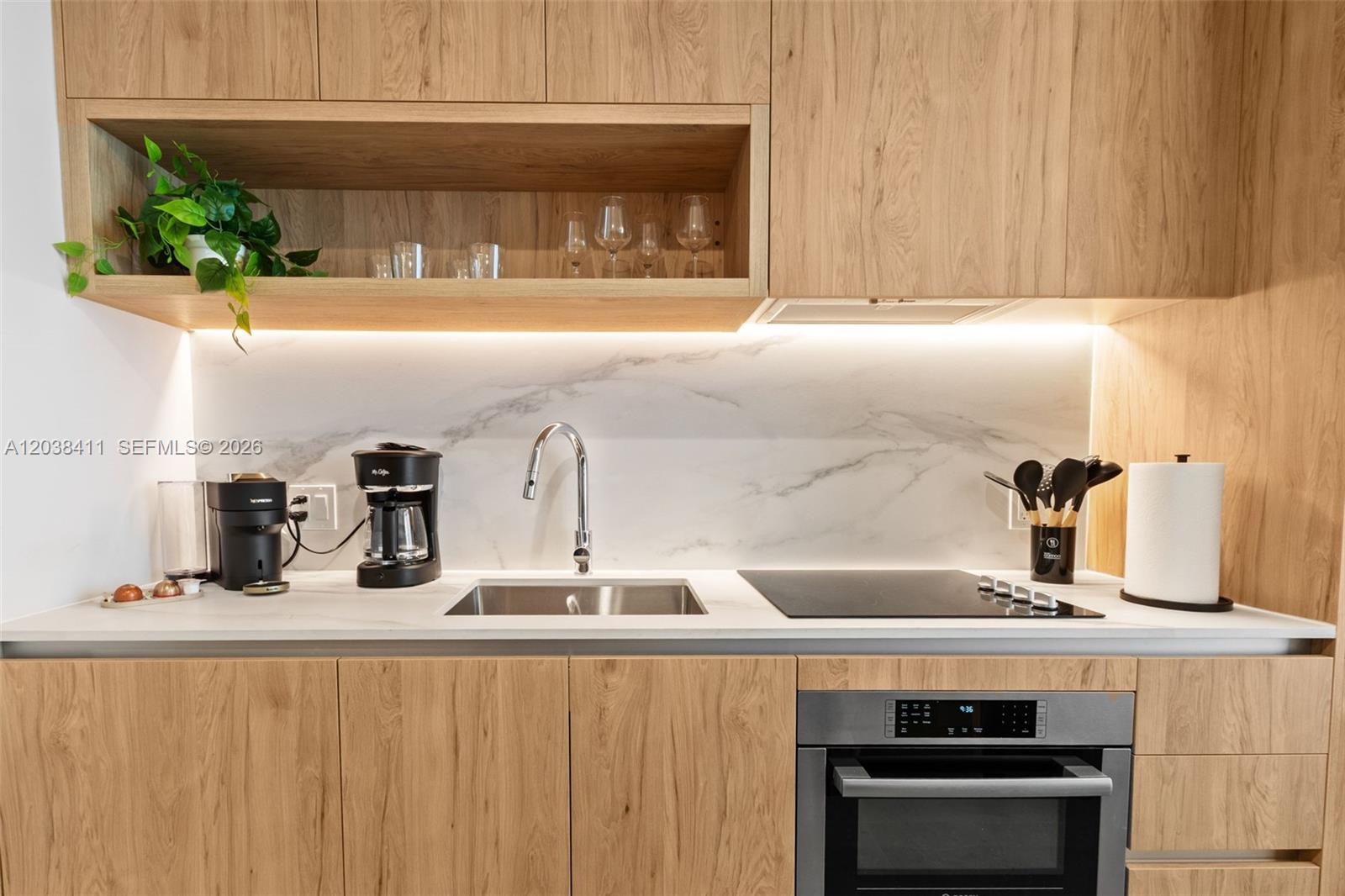 A modern kitchen features light wood cabinetry, a marble backsplash, and a stainless steel sink — 11 NE 6th St # 2406, Miami FL 33132, MIAMI, FL