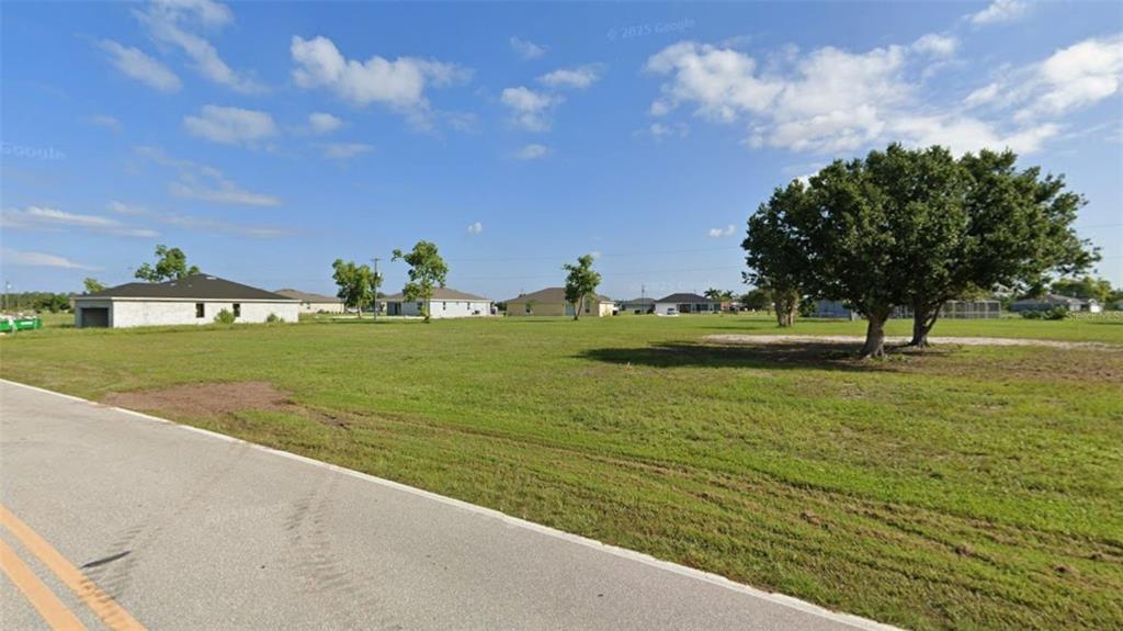 A grassy vacant lot with a few trees sits beside a paved road — 25142 ALCAZAR DRIVE, PUNTA GORDA, FL