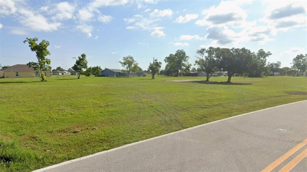 A grassy, vacant residential lot sits next to an asphalt road with houses in the background — 25142 ALCAZAR DRIVE, PUNTA GORDA, FL