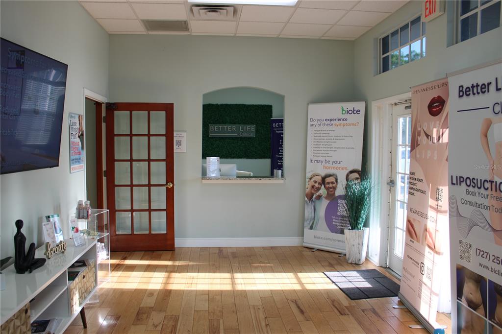 A bright clinic reception area features a wooden floor, a front desk, and promotional signage — 2835 ALT 19 HIGHWAY, PALM HARBOR, FL