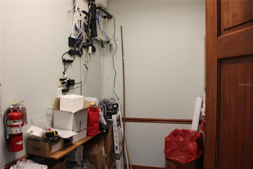 A utility closet features wall-mounted networking equipment, storage boxes, a fire extinguisher, and shelving — 2835 ALT 19 HIGHWAY, PALM HARBOR, FL