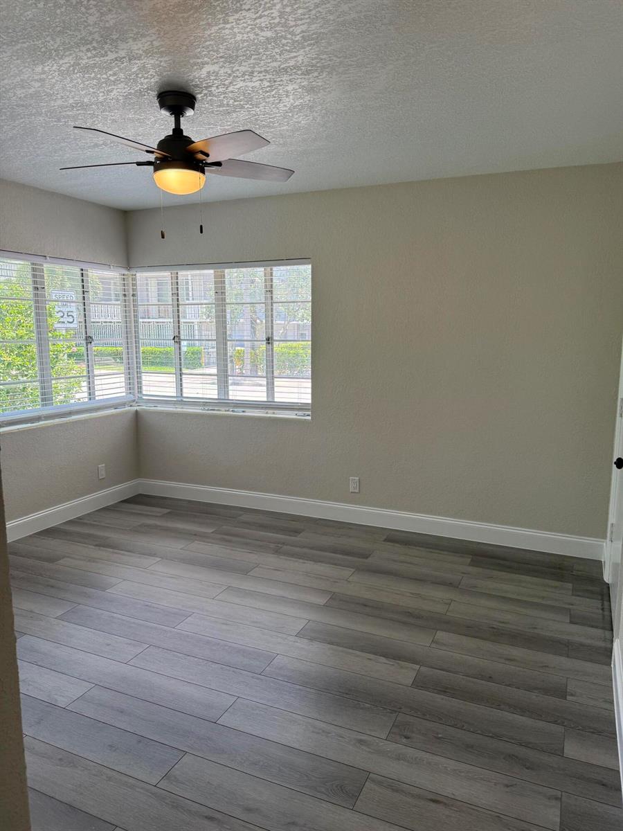 An empty room features light-colored walls, gray wood-look flooring, a ceiling fan, and corner windows — 112 Lake Avenue # 1, FL 33460, FL