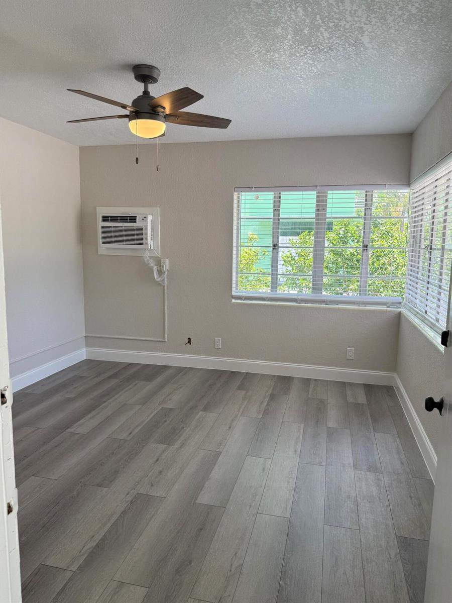 An empty bedroom features grey wood-look flooring, a ceiling fan, and a wall-mounted air conditioner — 112 Lake Avenue # 1, FL 33460, FL