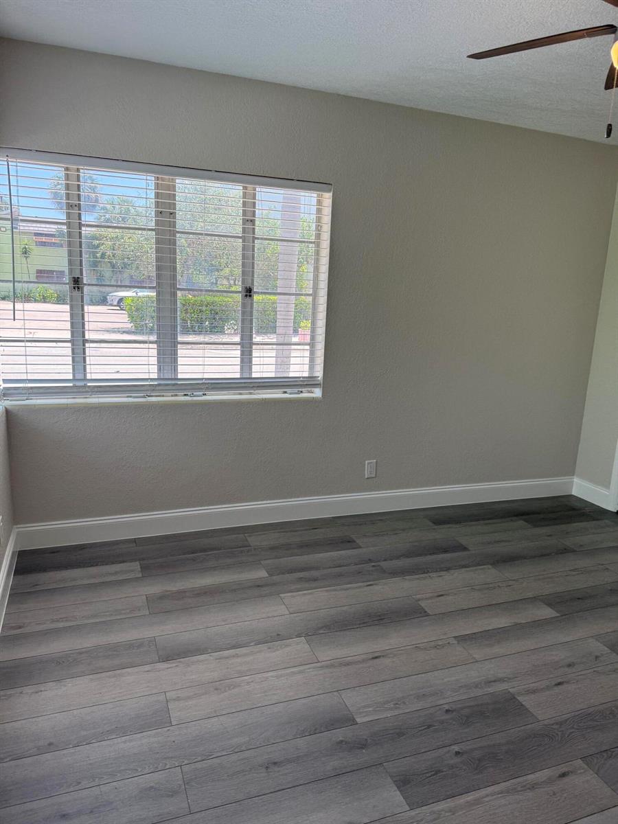 An empty room features gray wood-look flooring, beige walls, and a window with white blinds — 112 Lake Avenue # 1, FL 33460, FL