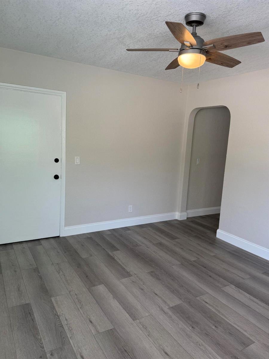 A room with gray wood-look flooring, a ceiling fan, a white door, and an arched doorway — 112 Lake Avenue # 1, FL 33460, FL