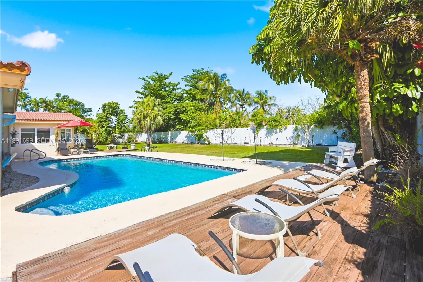 A backyard features a swimming pool, a wooden deck with lounge chairs, and palm trees — 9955 SW 74th St, Miami FL 33173, MIAMI, FL