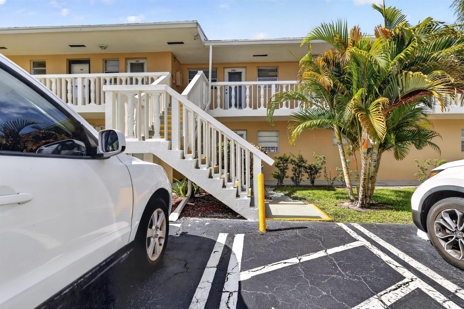 Exterior view of a two-story apartment building with white stairs and a palm tree — 2182 NE 1st Way # 202, Boynton Beach FL 33435, BOYNTON BEACH, FL
