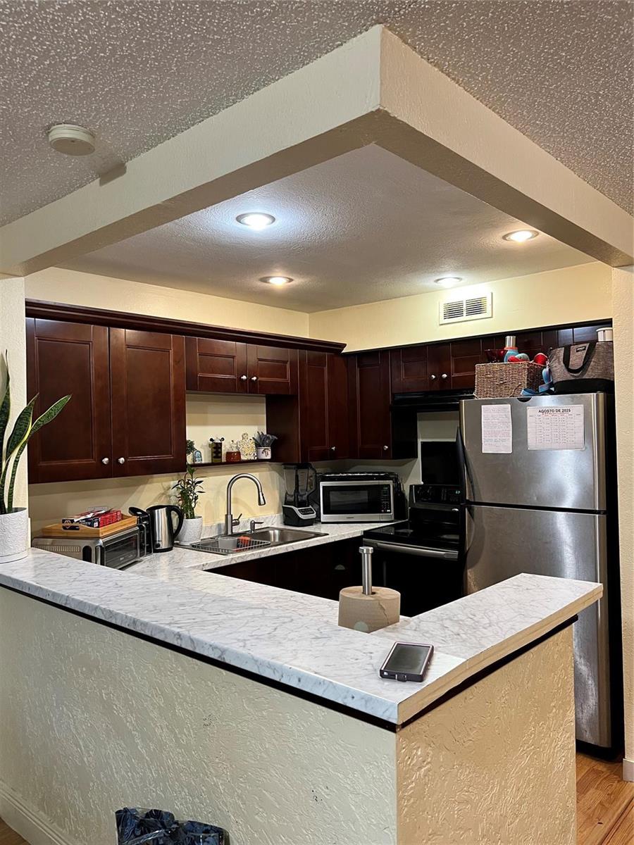 A kitchen features dark wood cabinets, white marble-patterned countertops, and stainless steel appliances — 708 SE 2nd Avenue # 428, Deerfield Beach FL 33441, DEERFIELD BEACH, FL