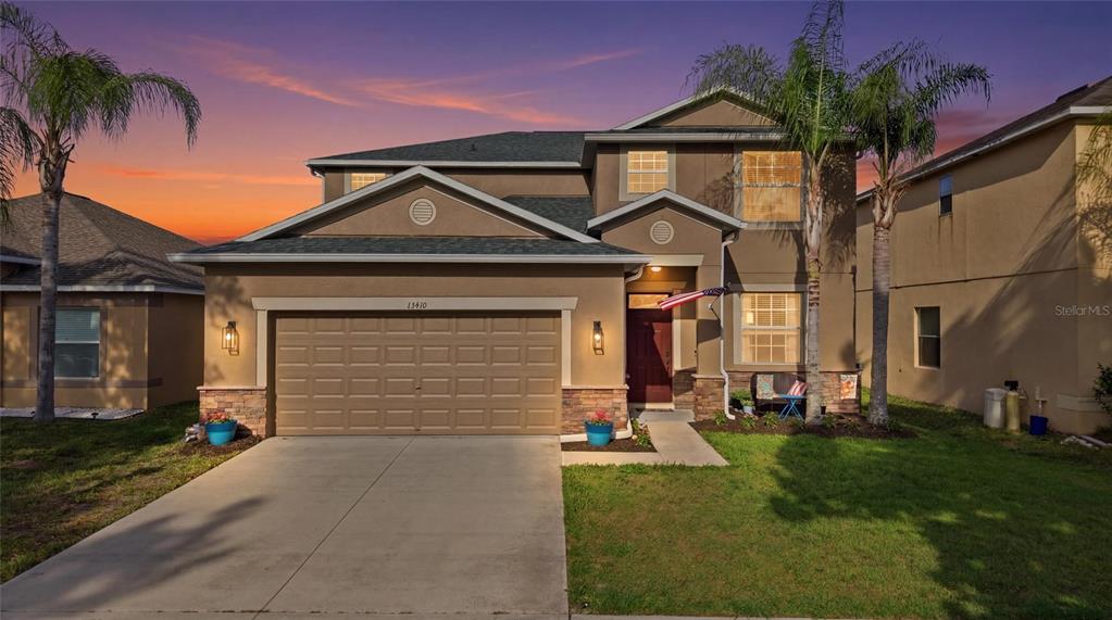 A two-story suburban house with a tan stucco exterior, a two-car garage, and palm trees — 15410 DAKOTA SKY PLACE, SUN CITY CENTER, FL