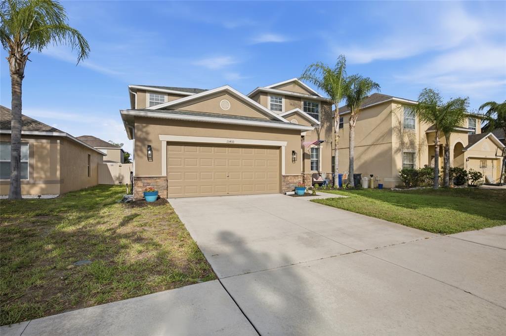 A two-story suburban house features a tan stucco exterior, a two-car garage, and palm trees — 15410 DAKOTA SKY PLACE, SUN CITY CENTER, FL