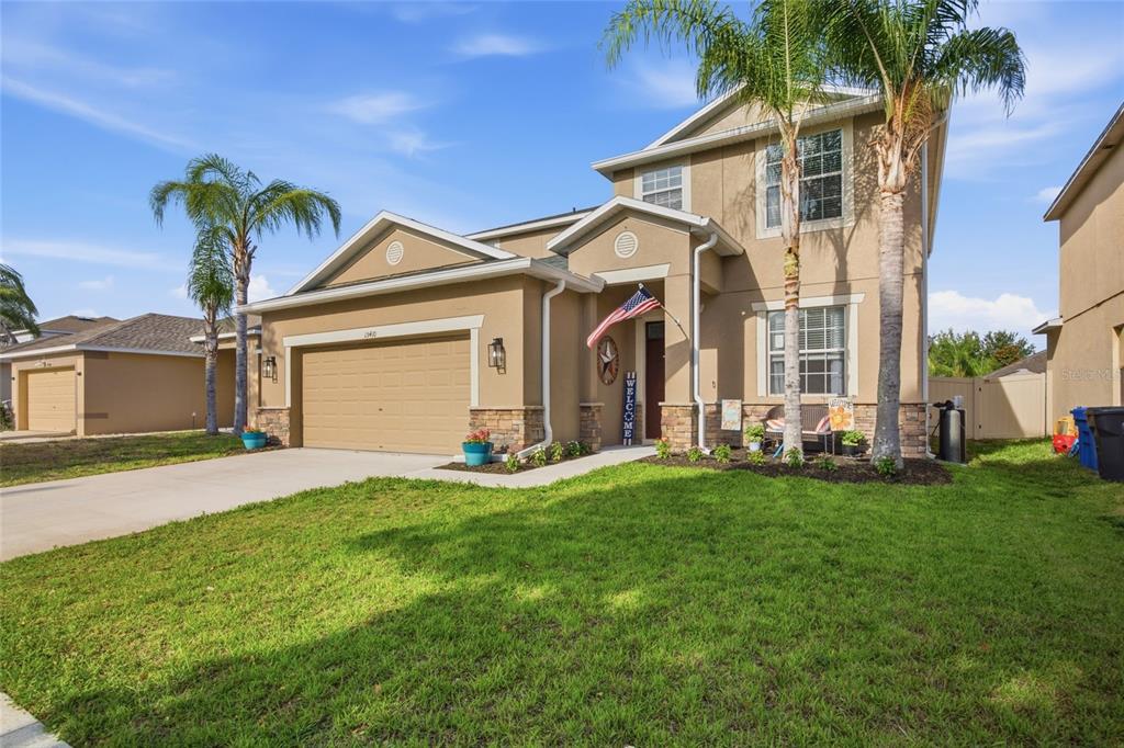 A two-story suburban house with a tan stucco exterior, a two-car garage, and palm trees — 15410 DAKOTA SKY PLACE, SUN CITY CENTER, FL
