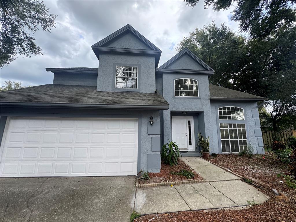 A two-story house with a gray stucco exterior, a white garage door, and arched windows — 1206 CORNERSTONE COURT, ORLANDO, FL