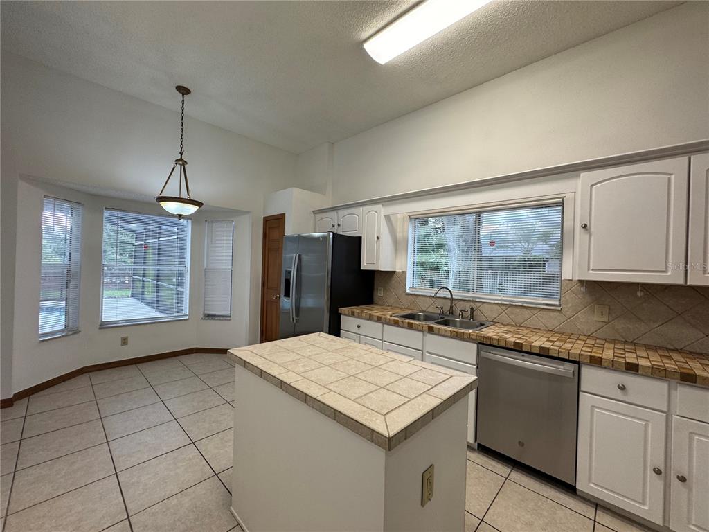 A kitchen features white cabinets, tiled countertops, a center island, and a breakfast nook area — 1206 CORNERSTONE COURT, ORLANDO, FL
