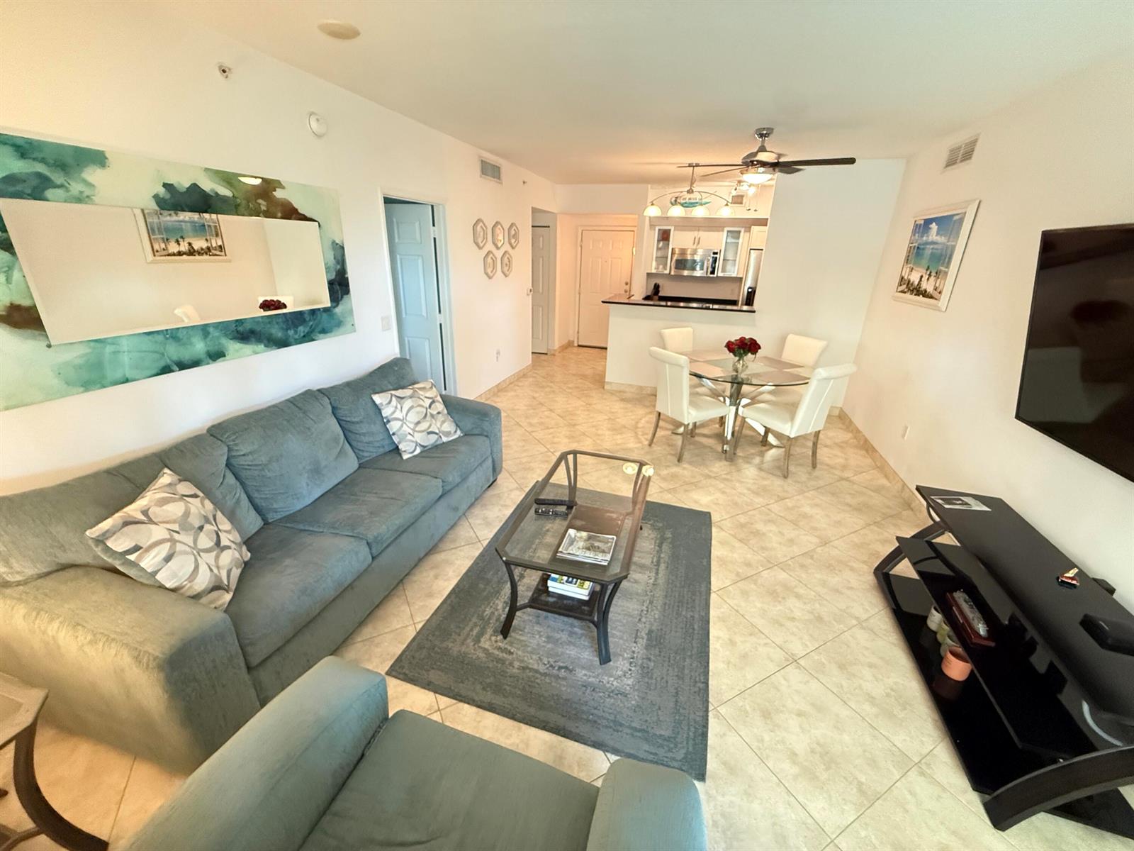 A living room with a blue sofa, glass coffee table, and dining area with kitchen — 700 E Boynton Beach Boulevard # 203, Boynton Beach FL 33435, BOYNTON BEACH, FL