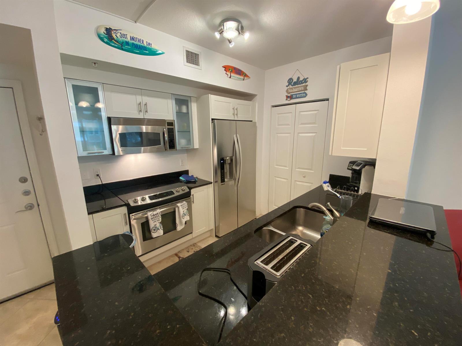 A kitchen features white cabinets, stainless steel appliances, and black granite countertops — 700 E Boynton Beach Boulevard # 203, Boynton Beach FL 33435, BOYNTON BEACH, FL