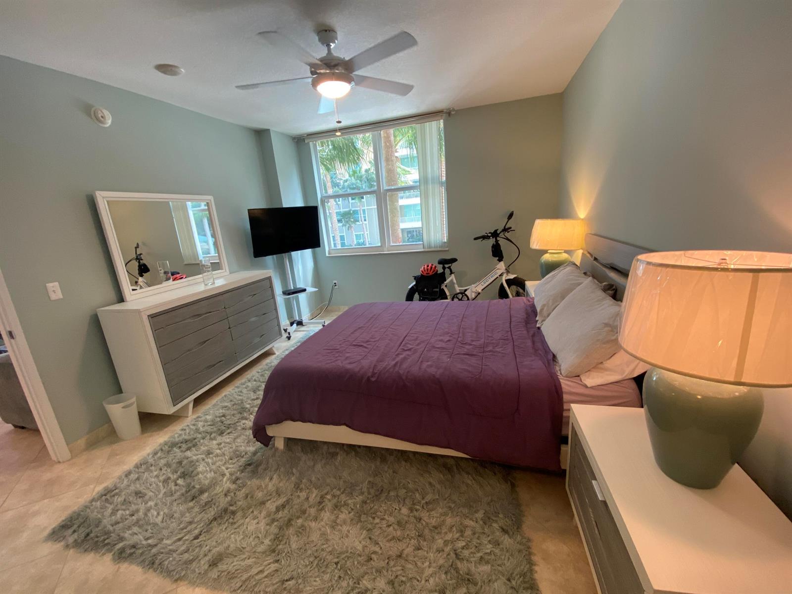 A bedroom features a purple bed, gray dresser, shag rug, and a bicycle by the window — 700 E Boynton Beach Boulevard # 203, Boynton Beach FL 33435, BOYNTON BEACH, FL