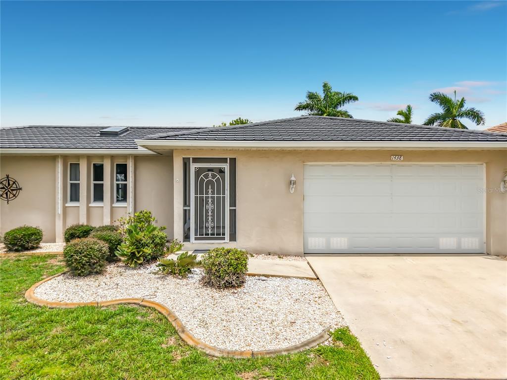 A single-story house exterior features a white garage, a screened front door, and landscaping — 1438 SEA FAN DRIVE, PUNTA GORDA, FL