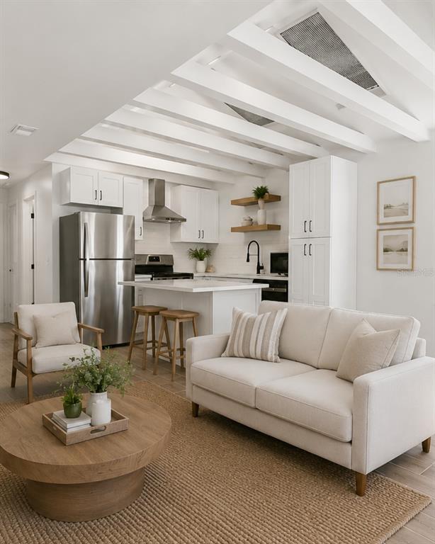 A bright, open-concept kitchen and living area features white cabinetry, exposed ceiling beams, and furniture — 1734 MARYLAND AVENUE NE, ST PETERSBURG, FL