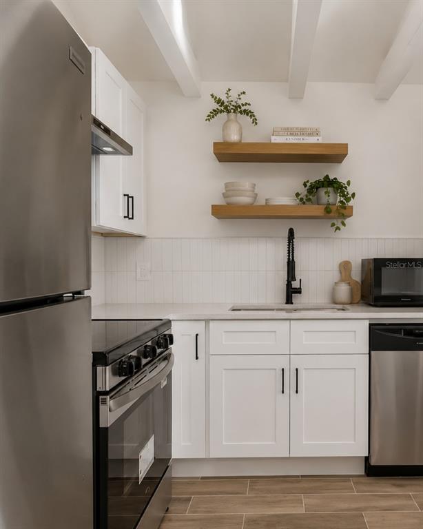 A kitchen features white cabinets, stainless steel appliances, open wood shelving, and a tiled backsplash — 1734 MARYLAND AVENUE NE, ST PETERSBURG, FL