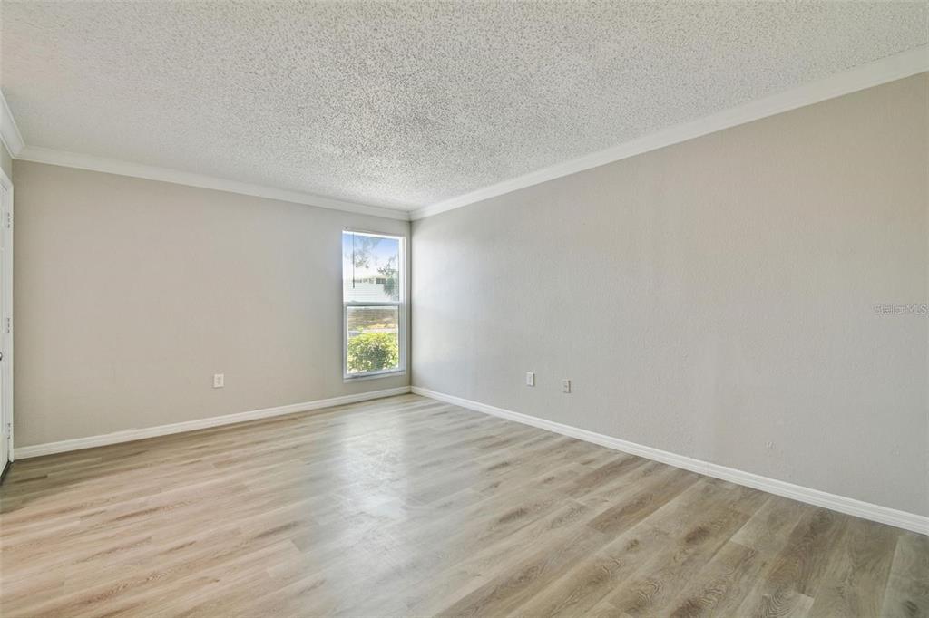 An empty room features light wood-look flooring, beige walls, a popcorn ceiling, and one window — 726 HAVEN PLACE UNIT 726, TARPON SPRINGS, FL