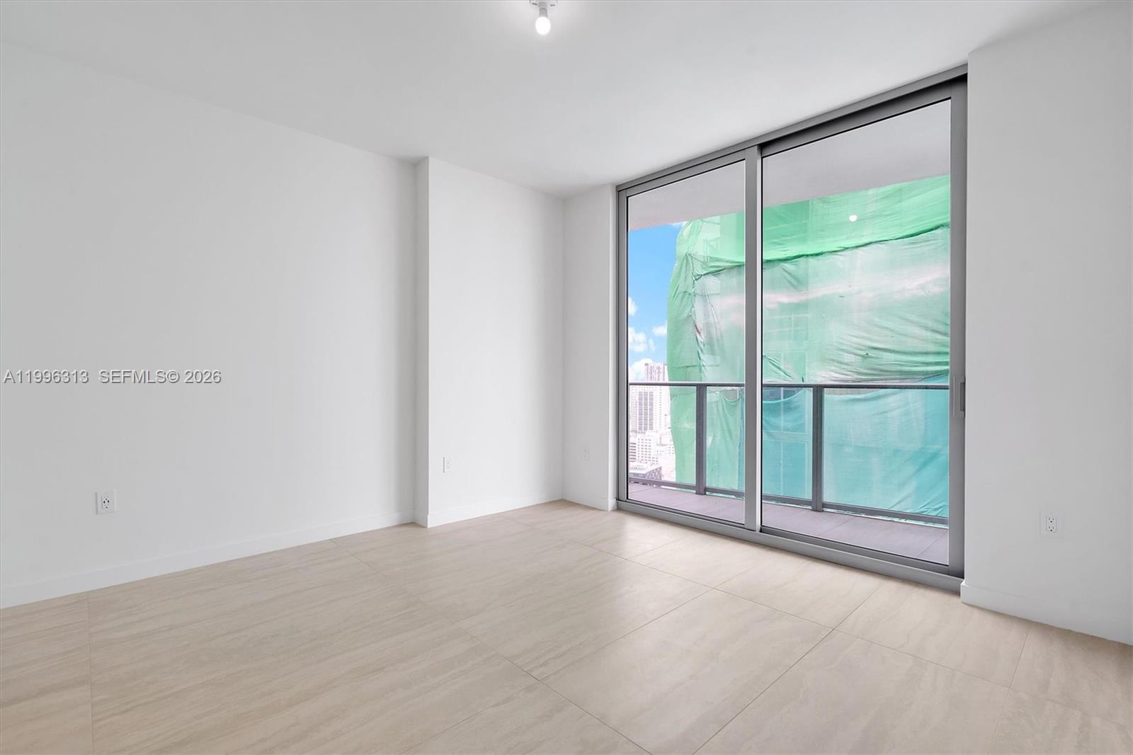 An empty room features light-colored tile flooring, white walls, and a sliding glass door balcony — 77 SE 5th Street # 4206, Miami FL 33131, MIAMI, FL