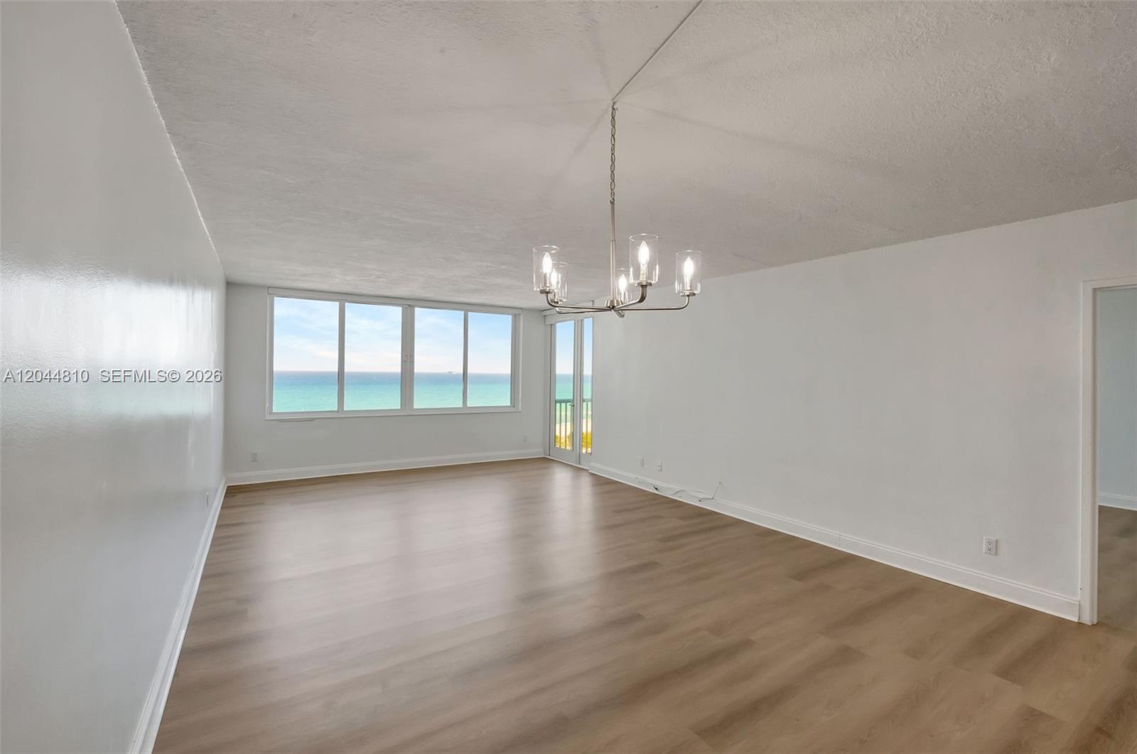 An empty living room features light wood-look flooring, white walls, and a view of the ocean — 5401 Collins Ave # 928, Miami Beach FL 33140, MIAMI BEACH, FL