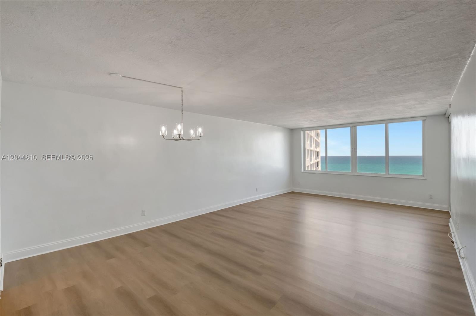An empty room features light wood-look flooring, white walls, a chandelier, and ocean views — 5401 Collins Ave # 928, Miami Beach FL 33140, MIAMI BEACH, FL