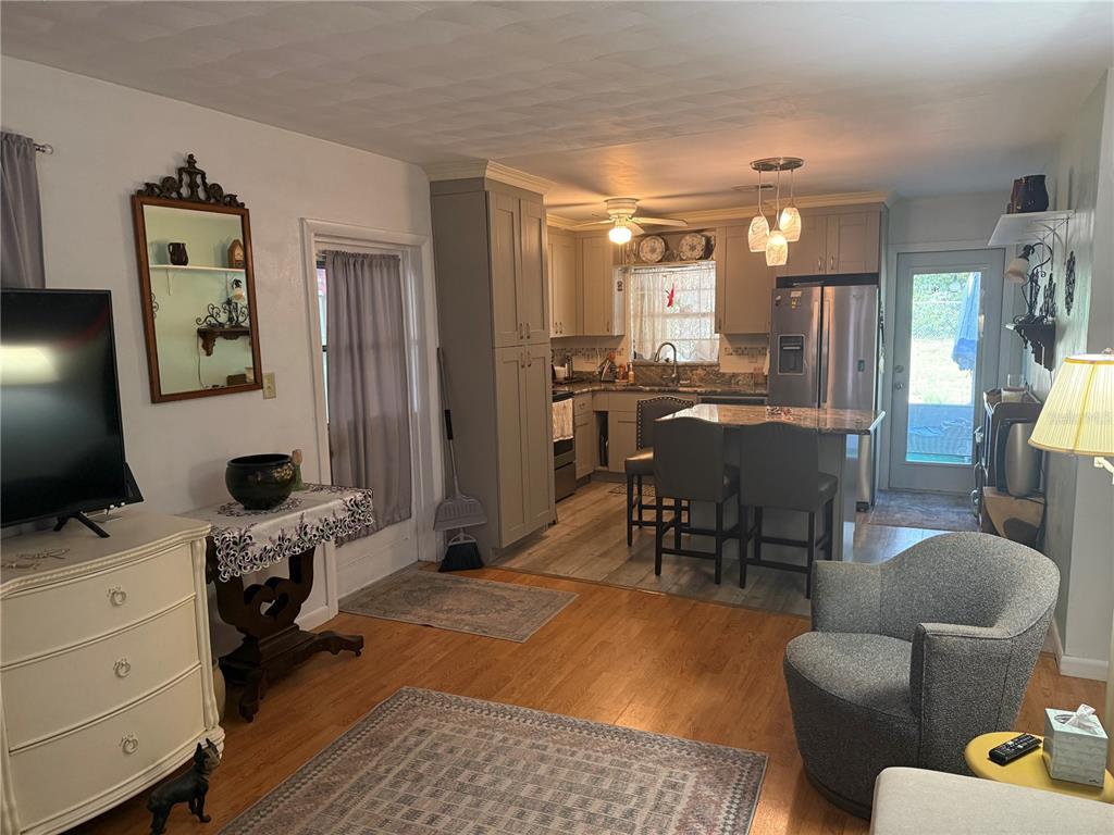 A kitchen with gray cabinets and an island opens into a living area with flooring — 37 PINE STREET, EUSTIS, FL